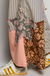Person wearing a striped shirt, floral scarf, pink pants, and patterned shoes on a plain background