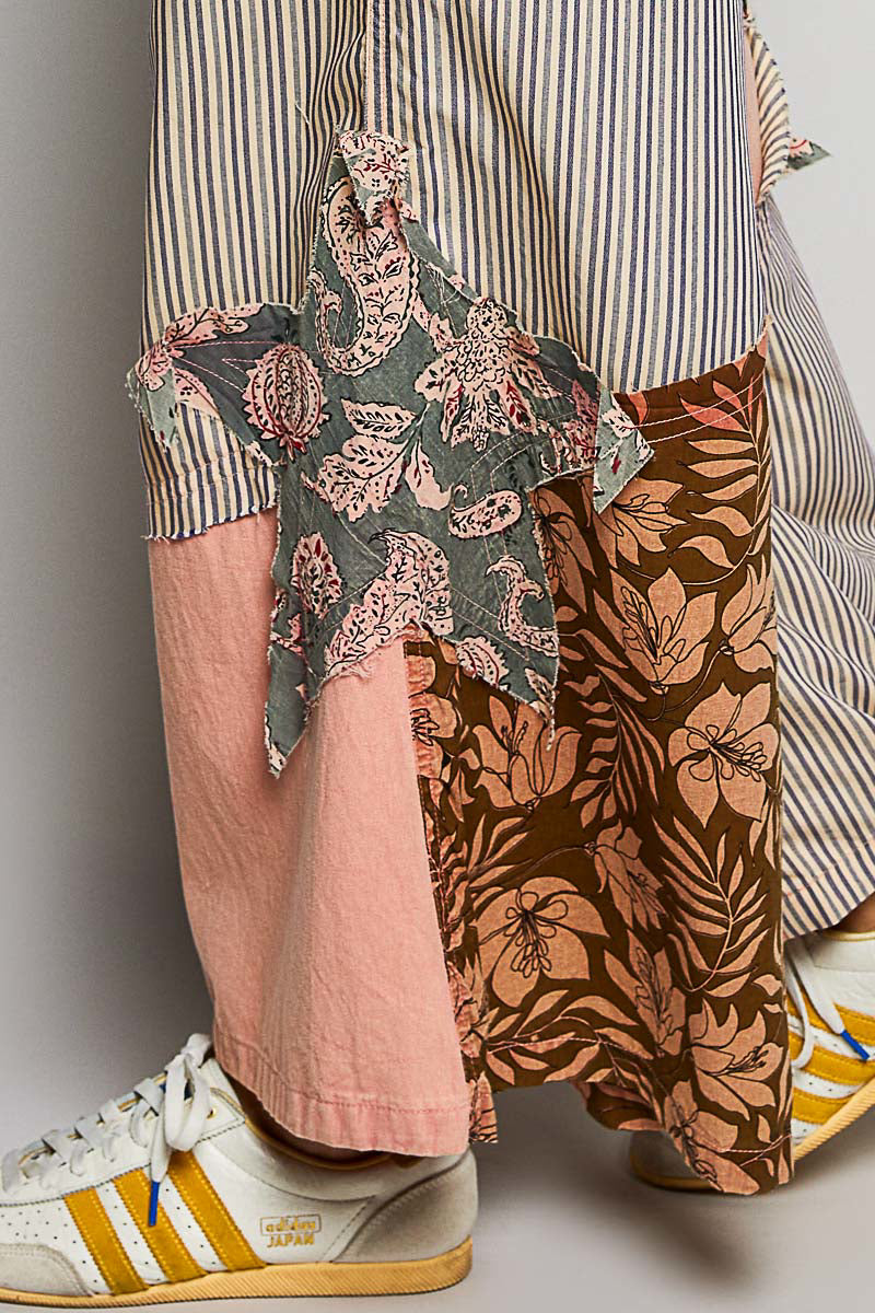 Person wearing a striped shirt, floral scarf, pink pants, and patterned shoes on a plain background