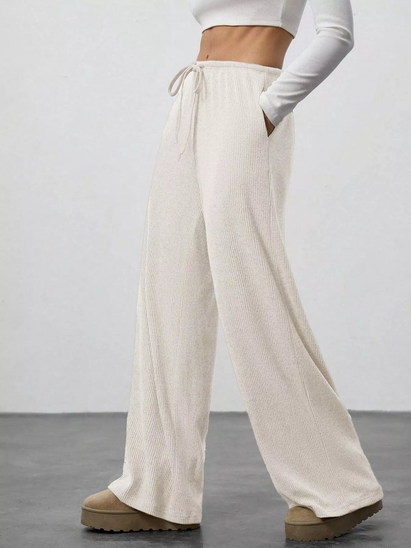 Beige wide-leg pants worn with a white top on a plain background
