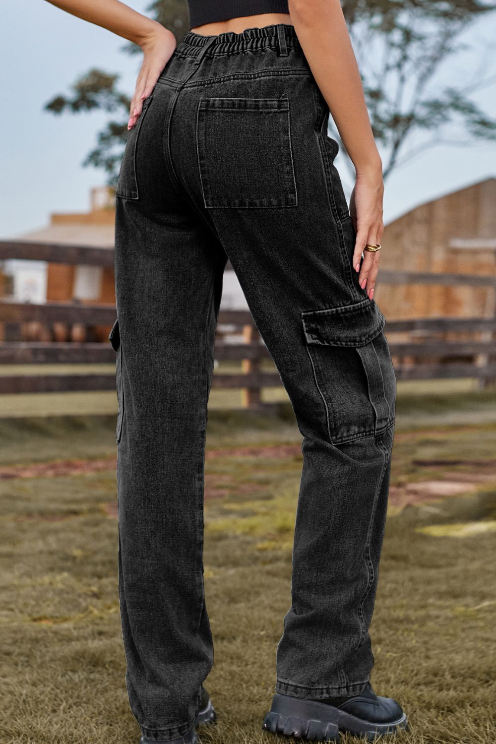 Person wearing black cargo pants in an outdoor setting with a wooden fence and grass.
