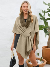 Woman wearing a beige poncho with a fur collar, standing in front of a white brick wall with potted plants.