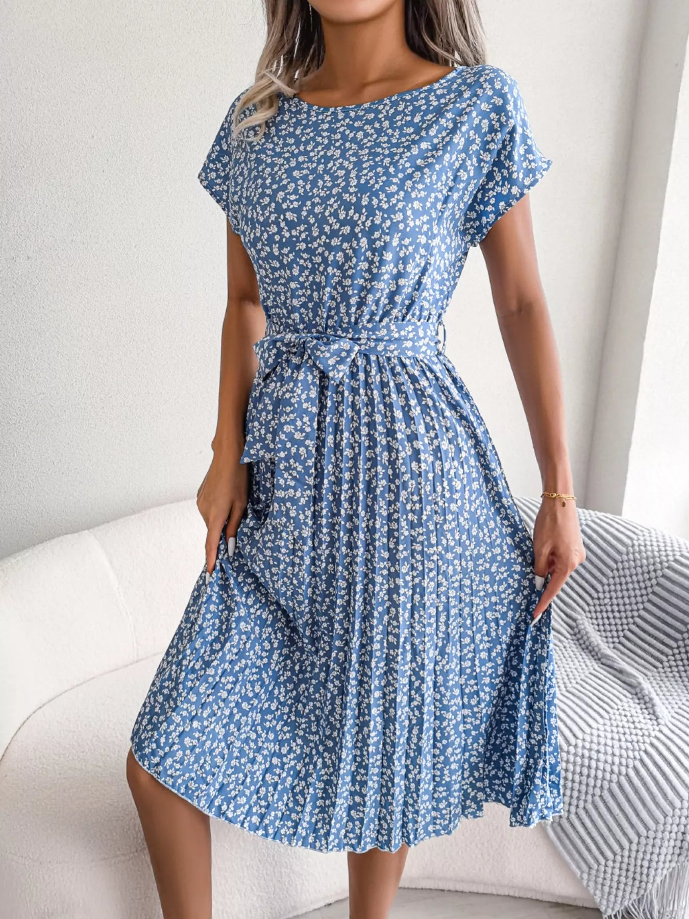 Woman wearing a blue floral dress sitting on a white couch.