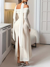 Woman wearing a white off-shoulder dress with a high slit in a minimalistic room.
