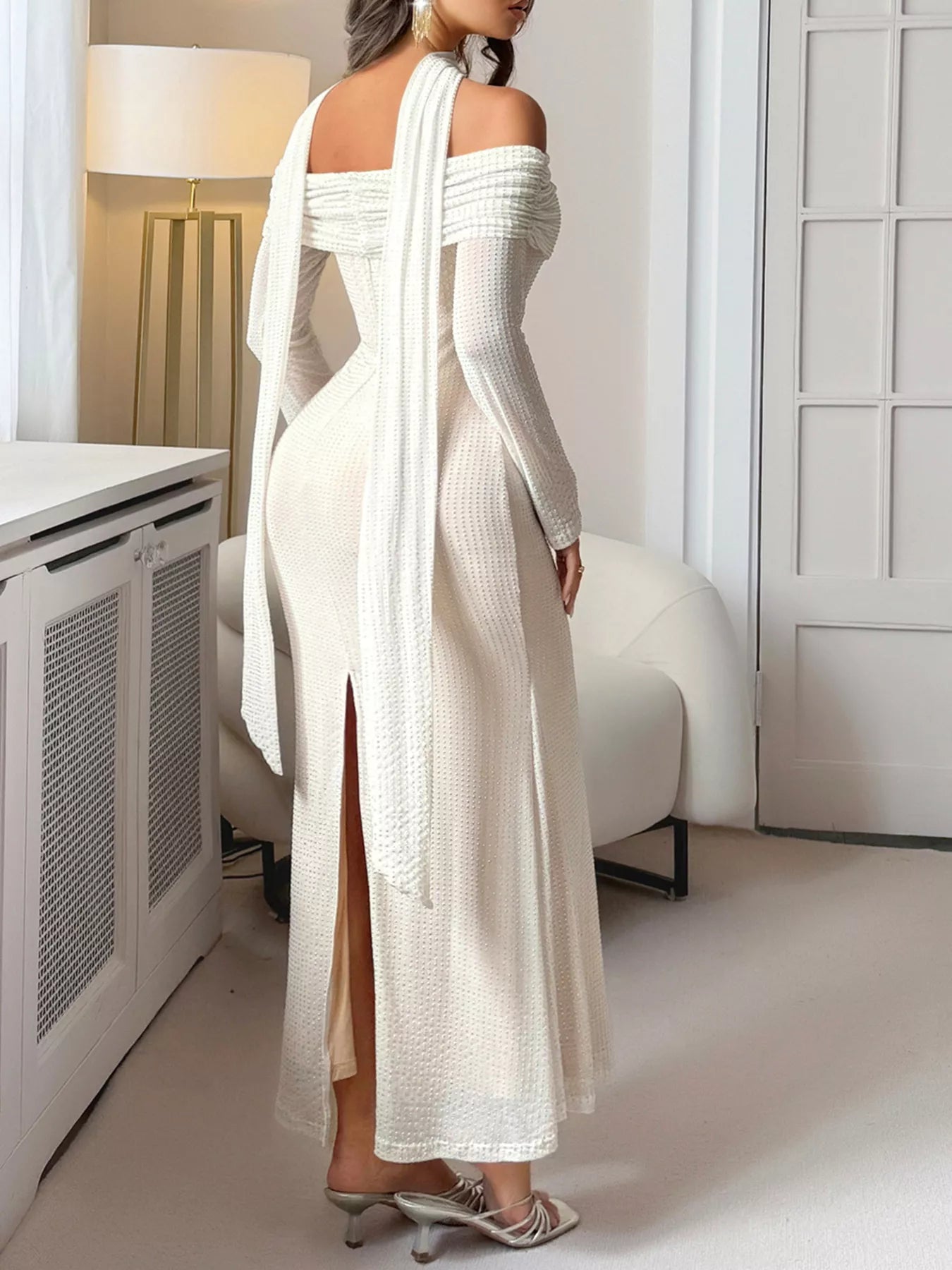 Woman wearing a white off-shoulder dress with a high slit in a minimalistic room.