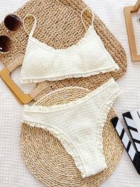 Cream-colored bikini set on a woven mat with sunglasses and a book.