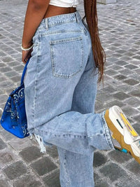 Person wearing light blue jeans and a white top, standing on a cobblestone street.