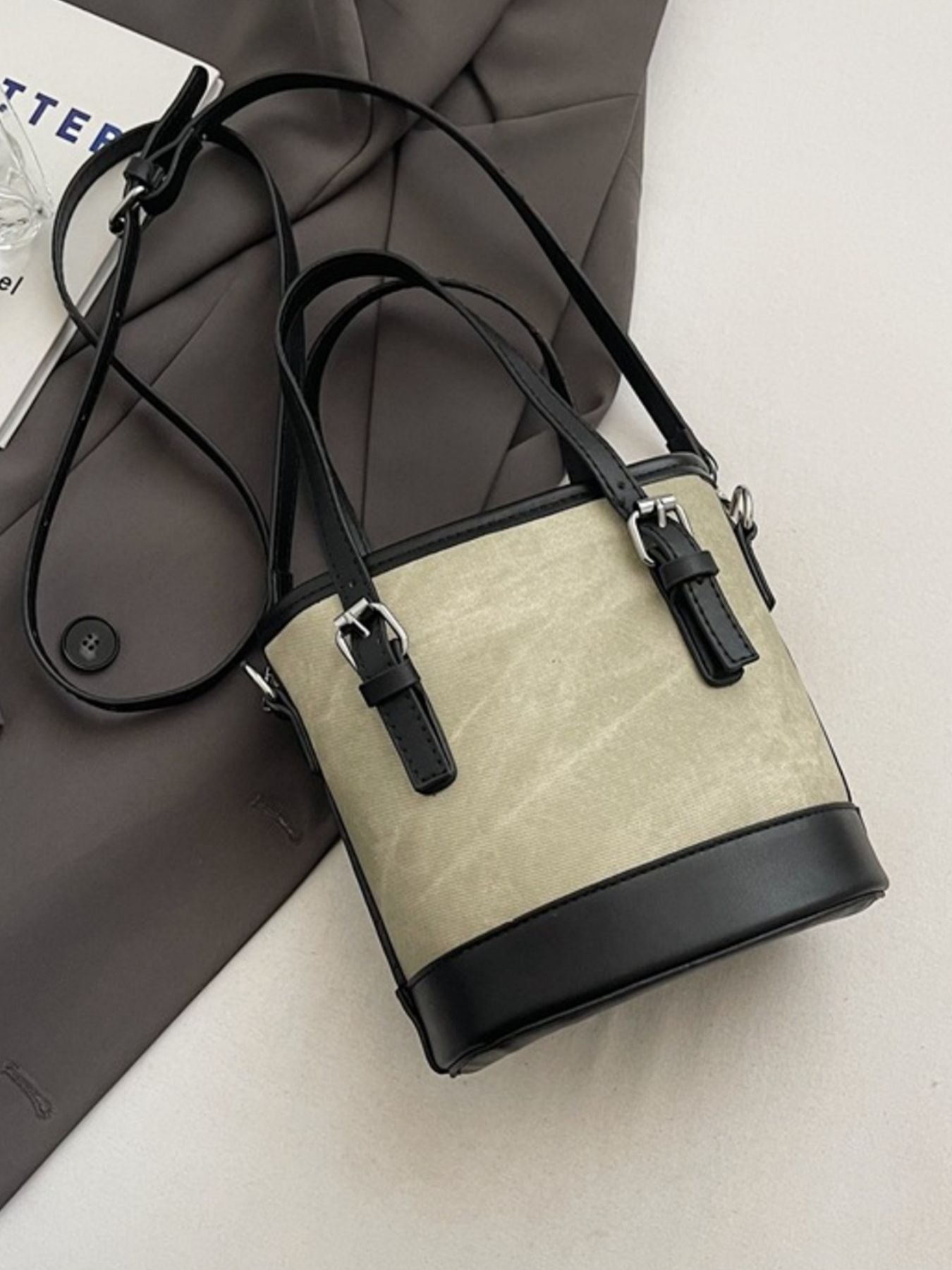 Small beige handbag with black accents on a light gray surface