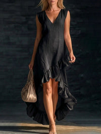 Woman wearing a black dress with ruffles holding a beige handbag against a dark background