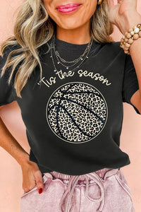 Woman wearing a black t-shirt with 'Tis the season' and leopard print design on a pink background