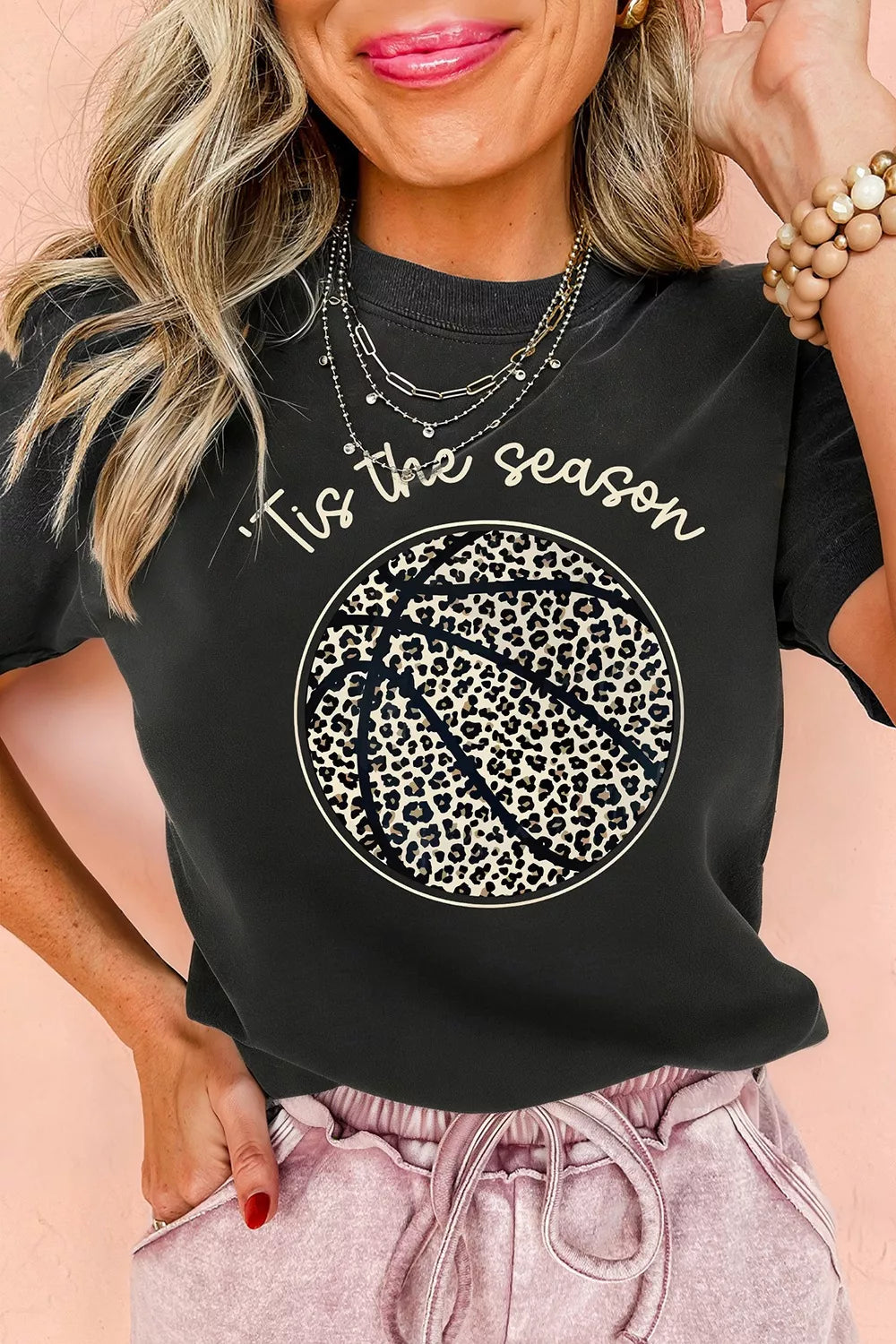 Woman wearing a black t-shirt with 'Tis the season' and leopard print design on a pink background