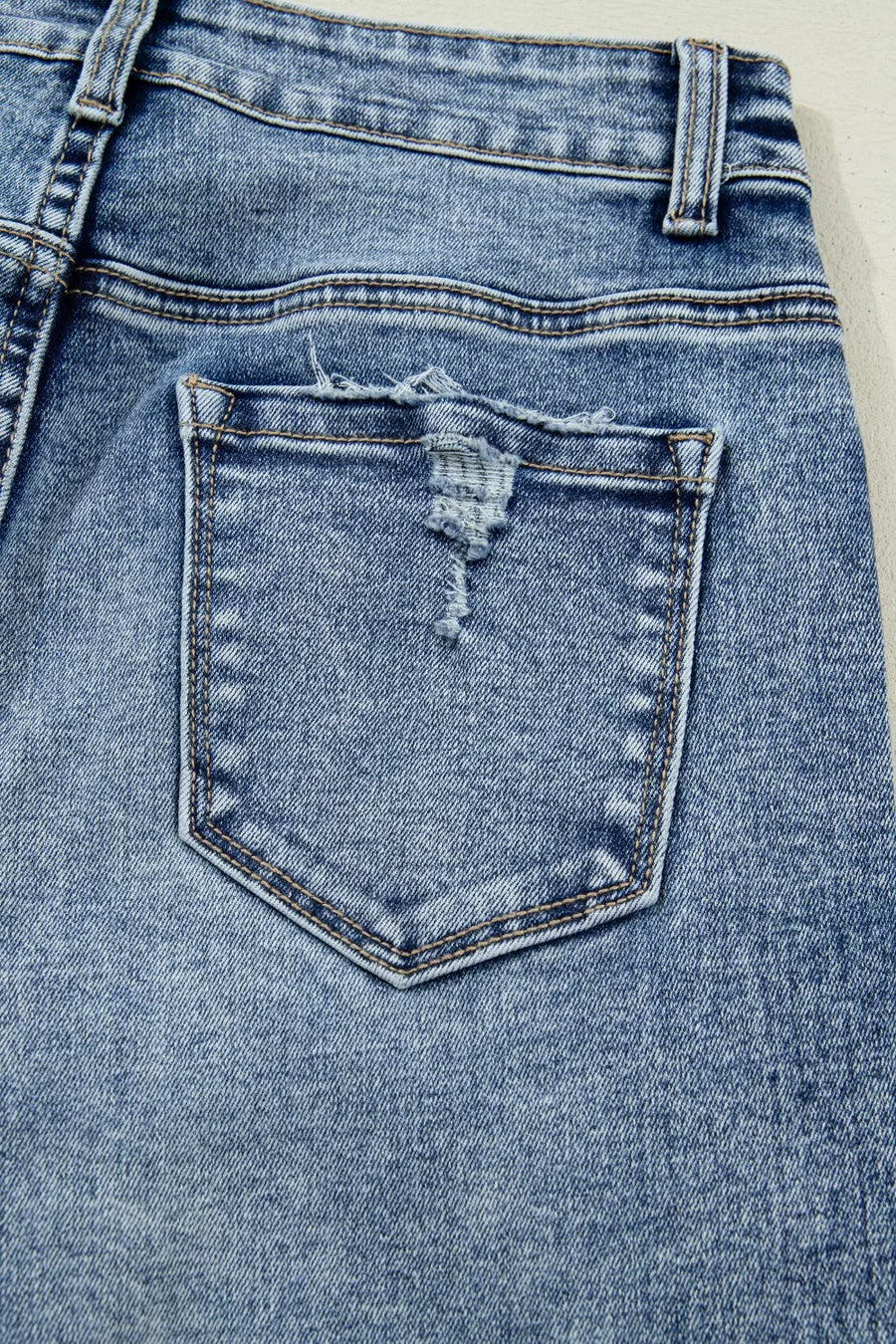 Close-up of a blue denim pocket with a slight tear on a white background