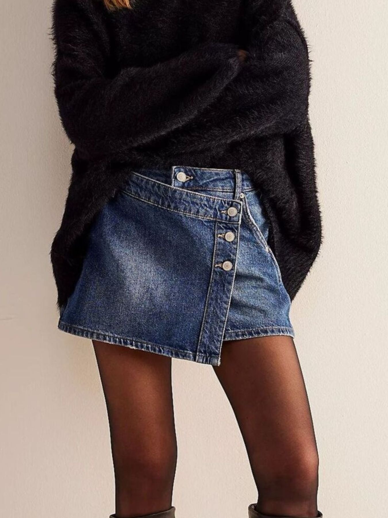 Person wearing a black oversized sweater and blue denim skirt on a plain background