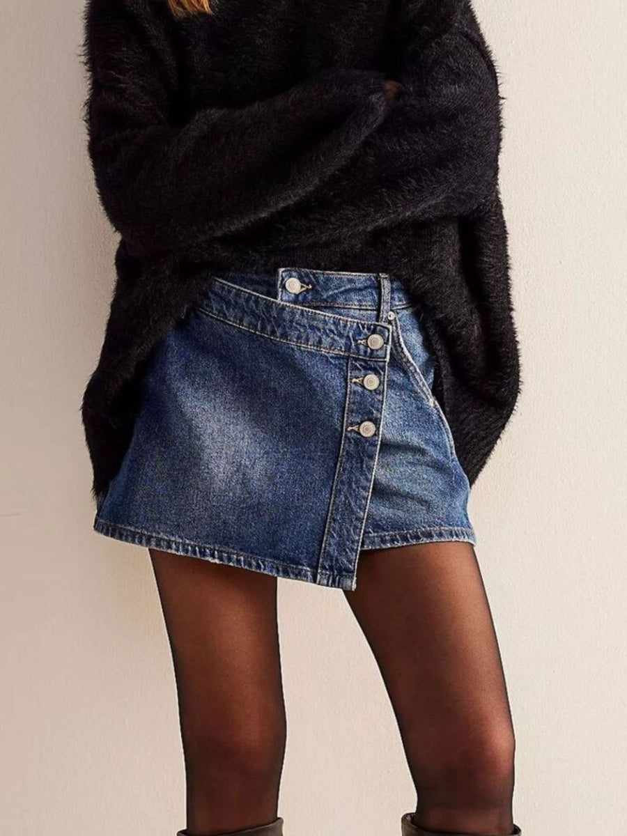Person wearing a black oversized sweater and blue denim skirt on a plain background