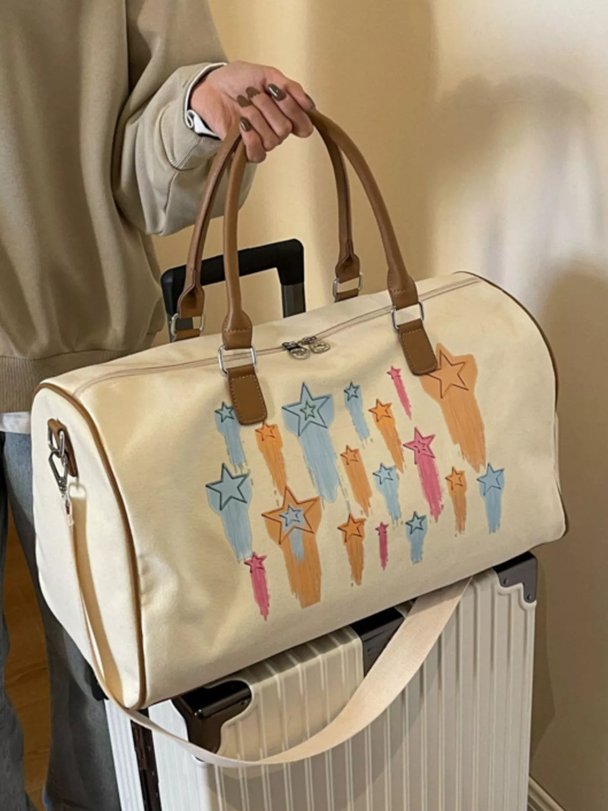 Beige duffel bag with star designs held by a person next to a suitcase.