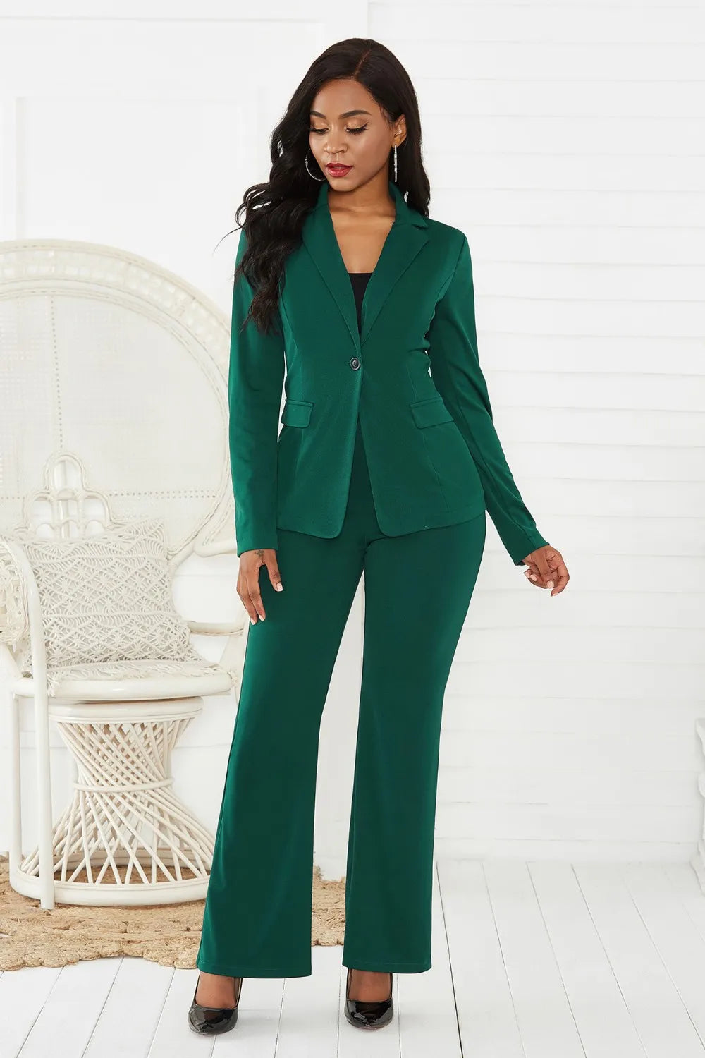 Woman wearing a green suit standing in a minimalistic room with a white chair.