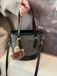 Gray handbag with a fluffy keychain held by a person against a neutral background