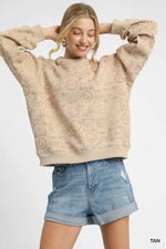 Woman wearing a beige textured sweatshirt and denim shorts on a white background