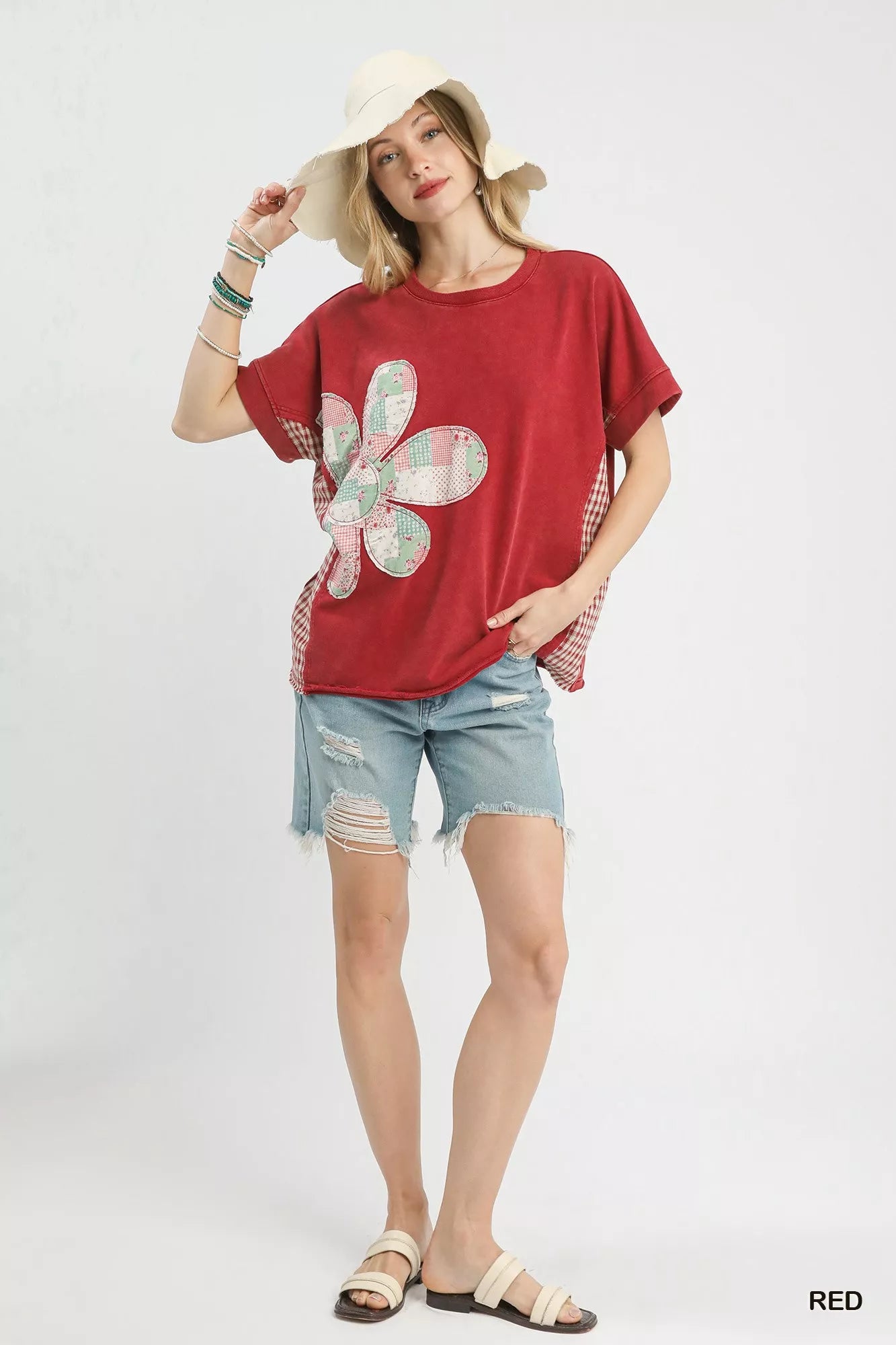 Woman wearing a red t-shirt with a flower design, denim shorts, and a hat on a white background