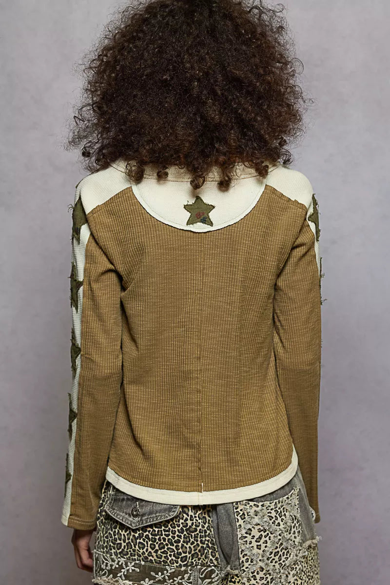 Person wearing a brown jacket with a star patch on the back against a gray background