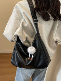 Person wearing a black shoulder bag with a fluffy white keychain, standing against a neutral background.