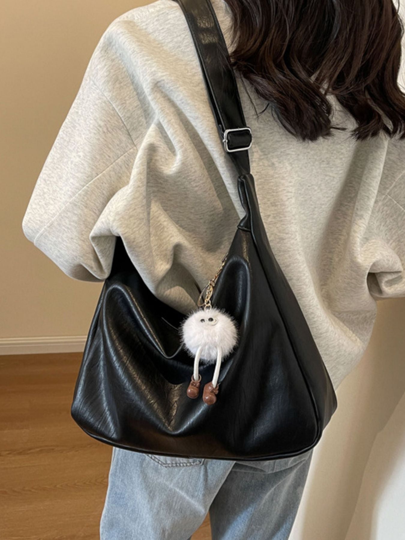Person wearing a black shoulder bag with a fluffy white keychain, standing against a neutral background.