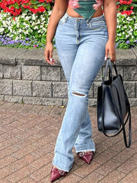 Person wearing light blue jeans with a black handbag in front of a floral background