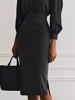 Person wearing a black dress holding a black handbag against a white wall.