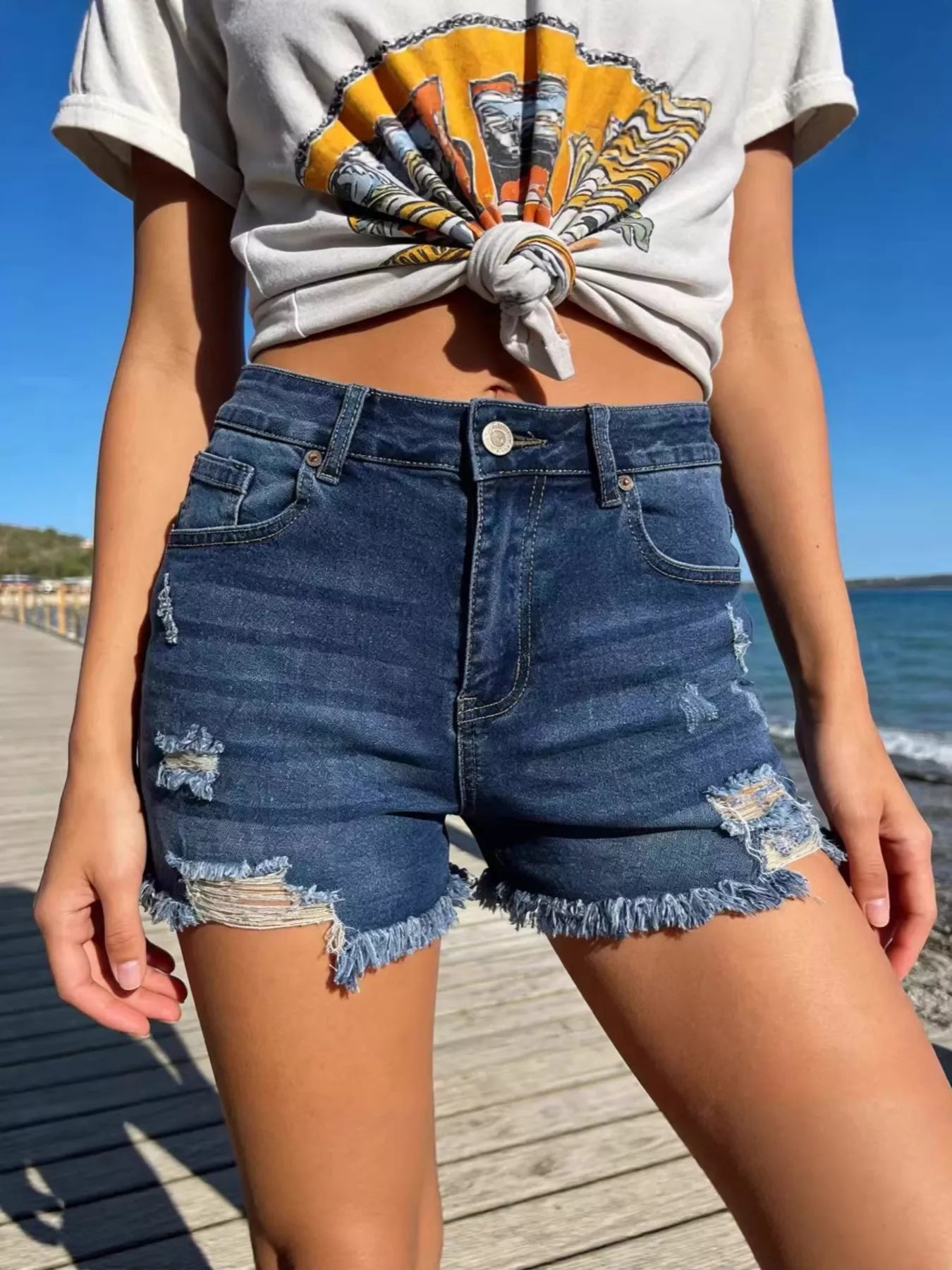 Person wearing a graphic t-shirt and denim shorts by the beach
