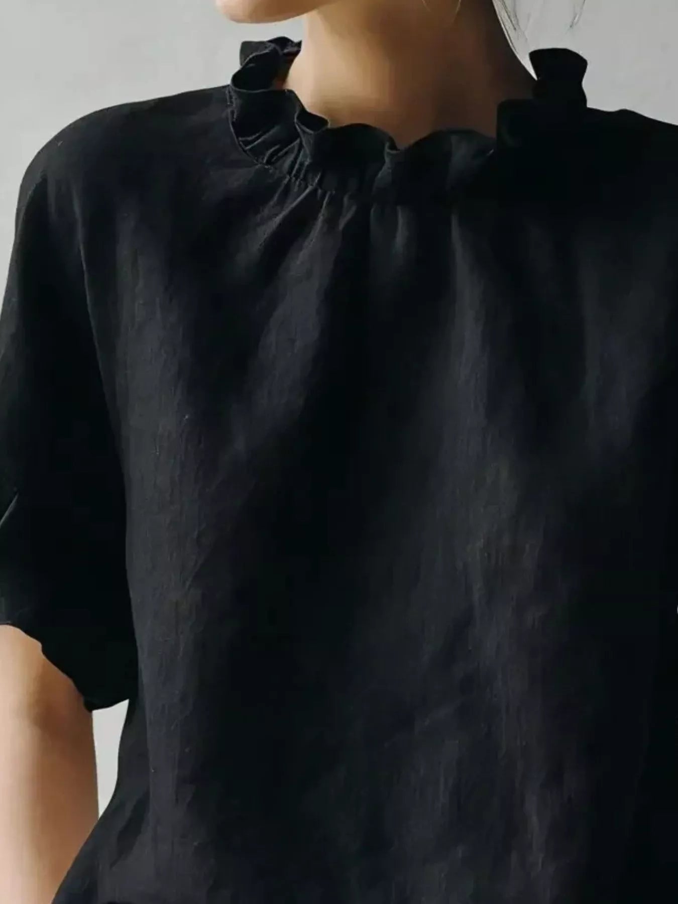 Close-up of a person wearing a black top with a ruffled neckline against a neutral background