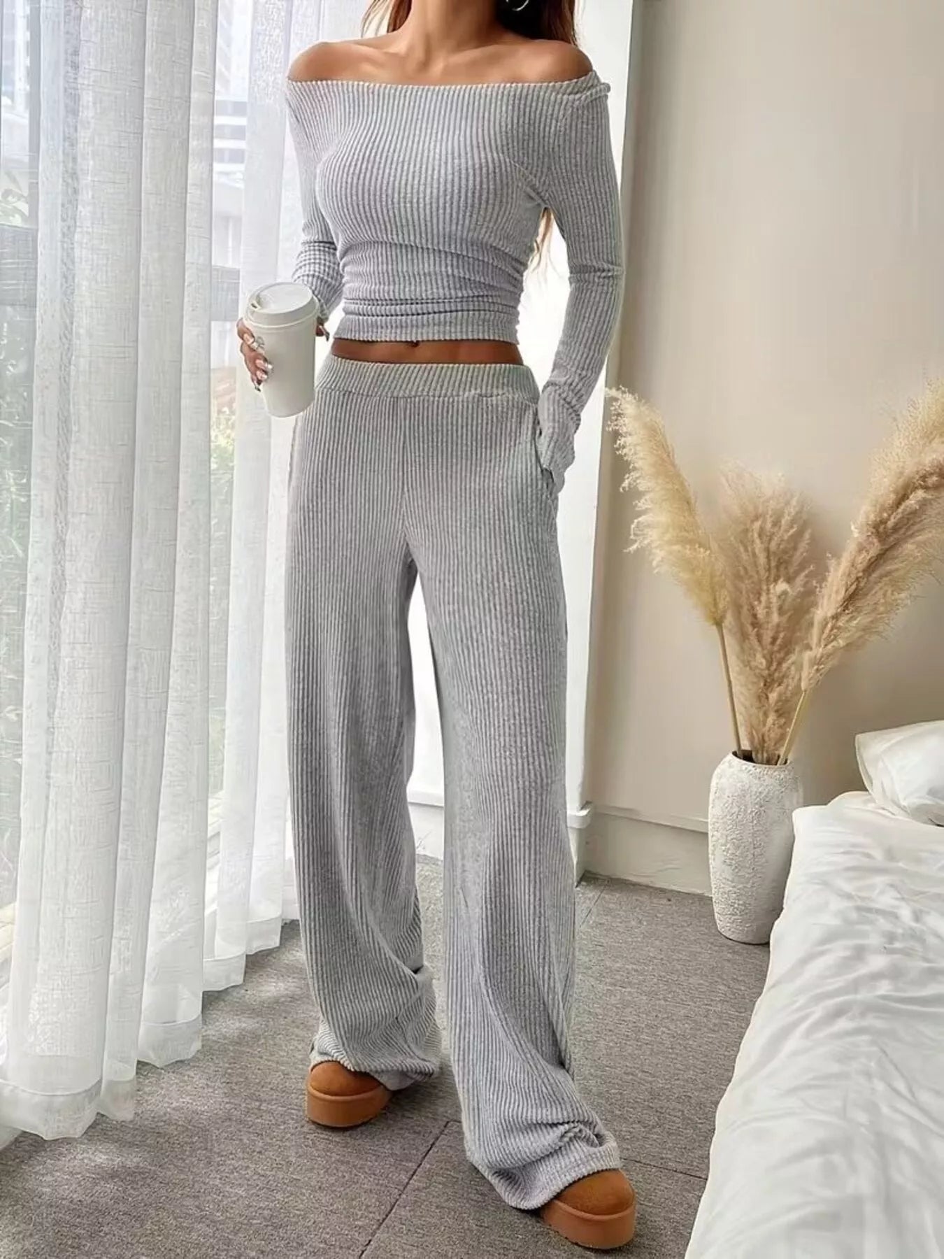 Person wearing a gray ribbed sweater and pants in a bedroom setting.