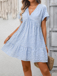 Woman wearing a blue and white checkered dress against a light gray wall.