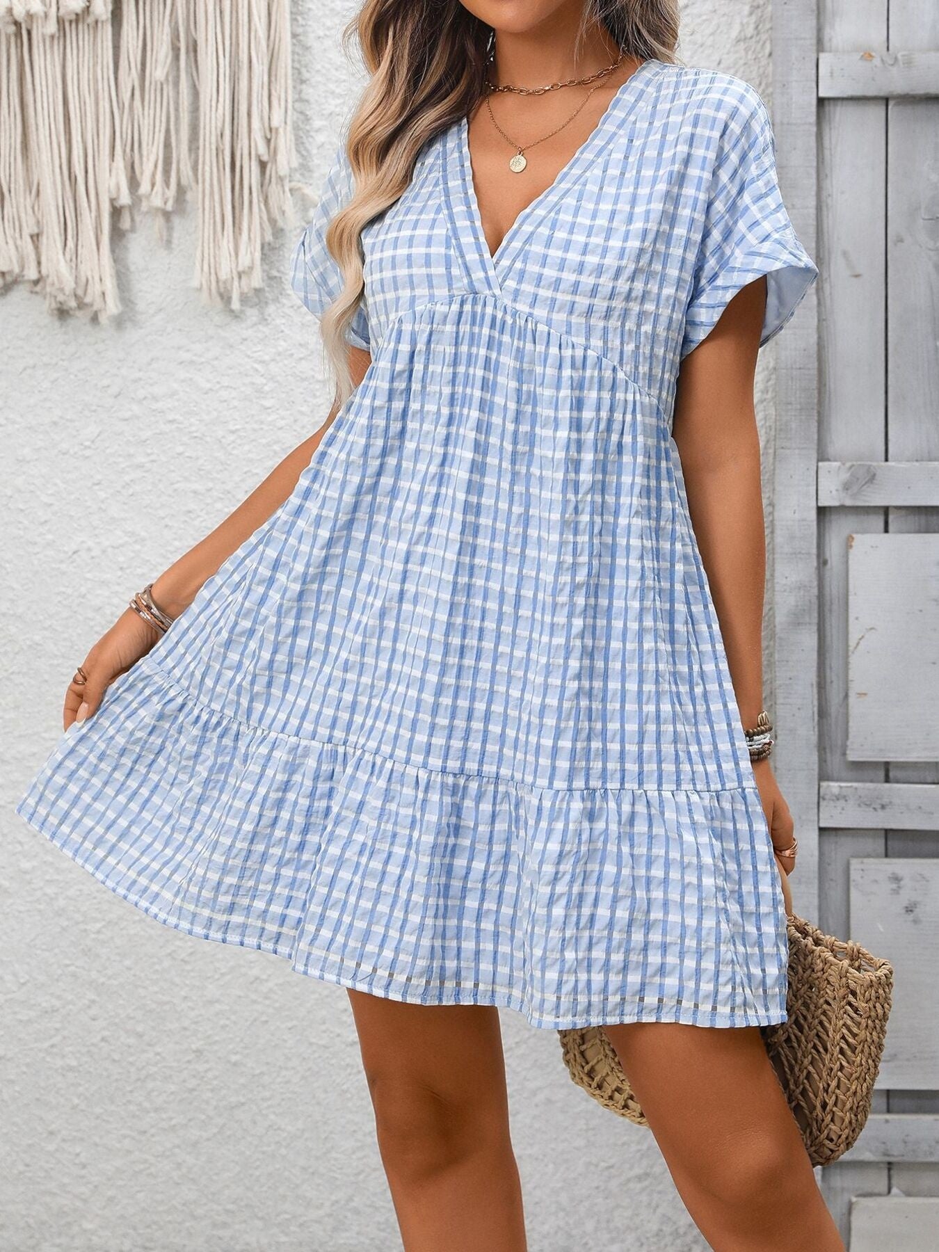 Woman wearing a blue and white checkered dress against a light gray wall.
