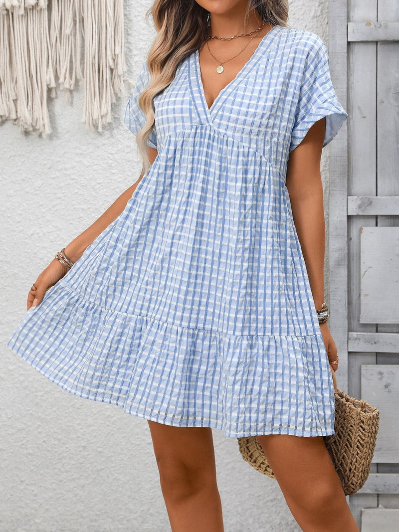 Woman wearing a blue and white checkered dress against a light gray wall.