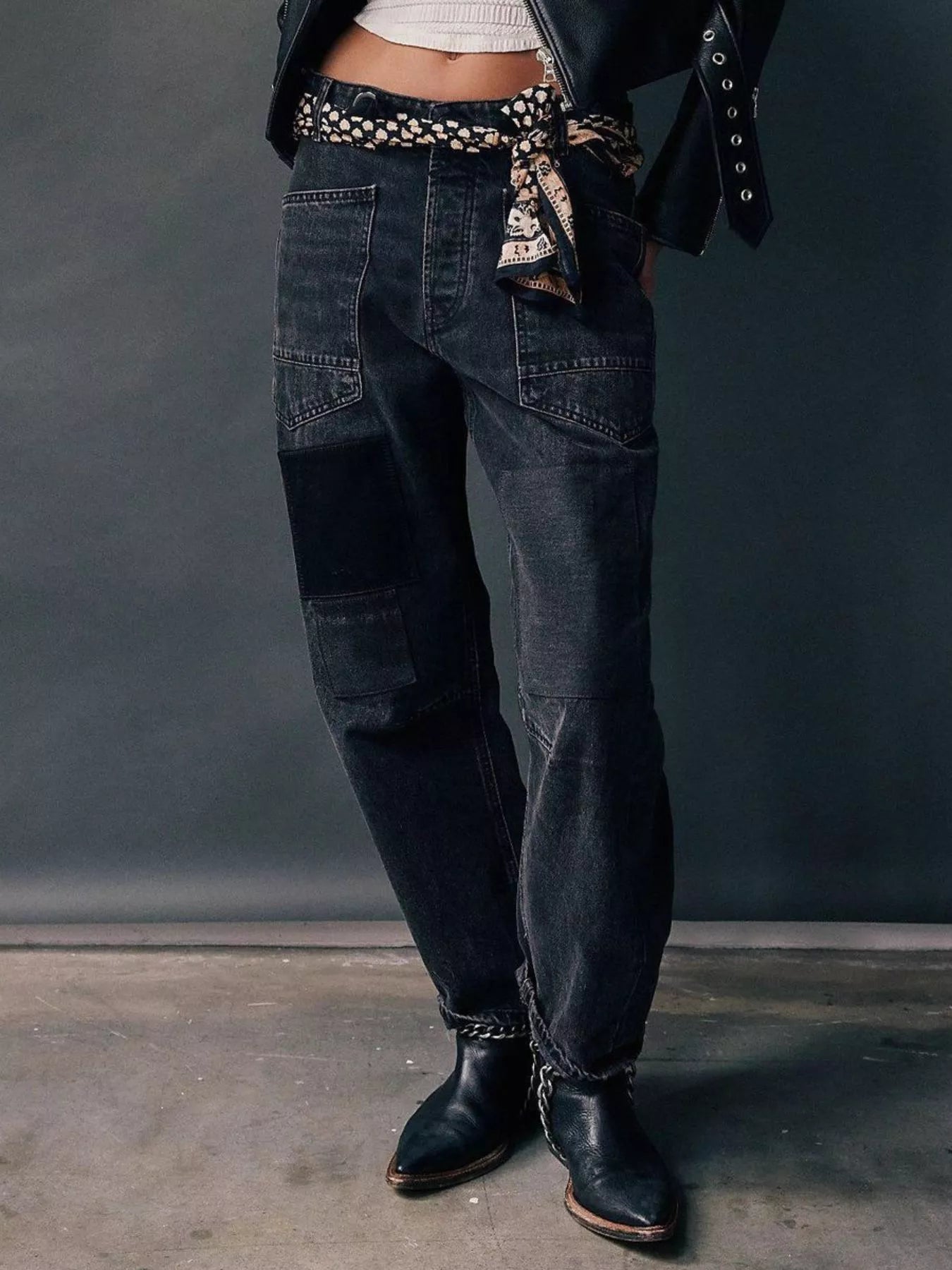 Person wearing dark blue jeans with a patterned belt against a gray background