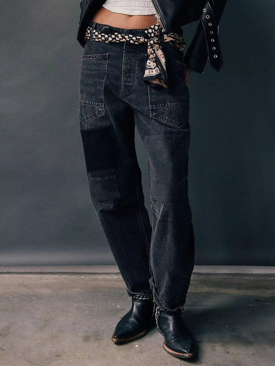 Person wearing dark blue jeans with a patterned belt against a gray background