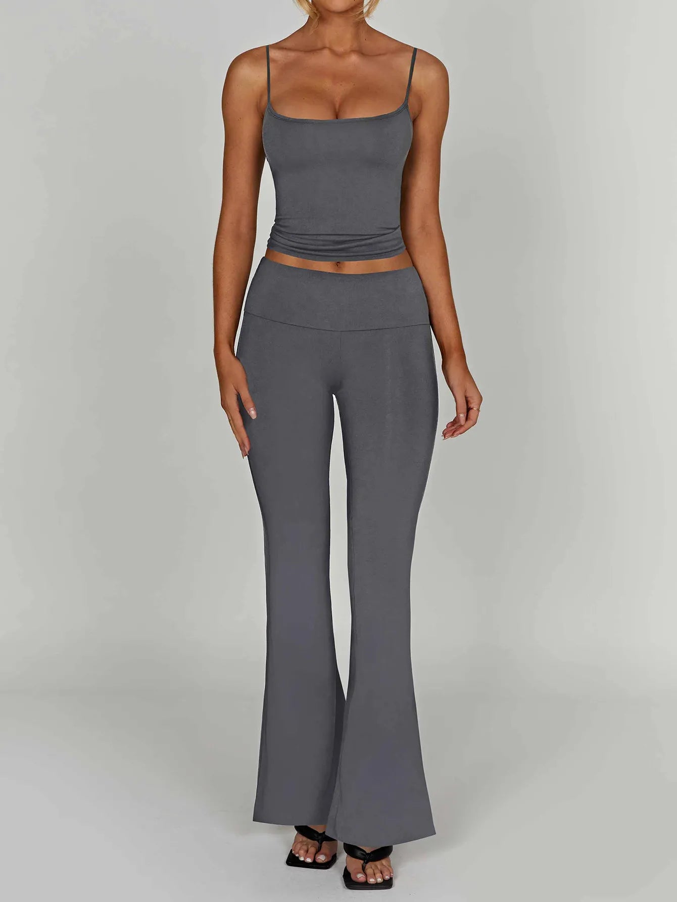 Woman wearing a gray tank top and high-waisted leggings on a plain background
