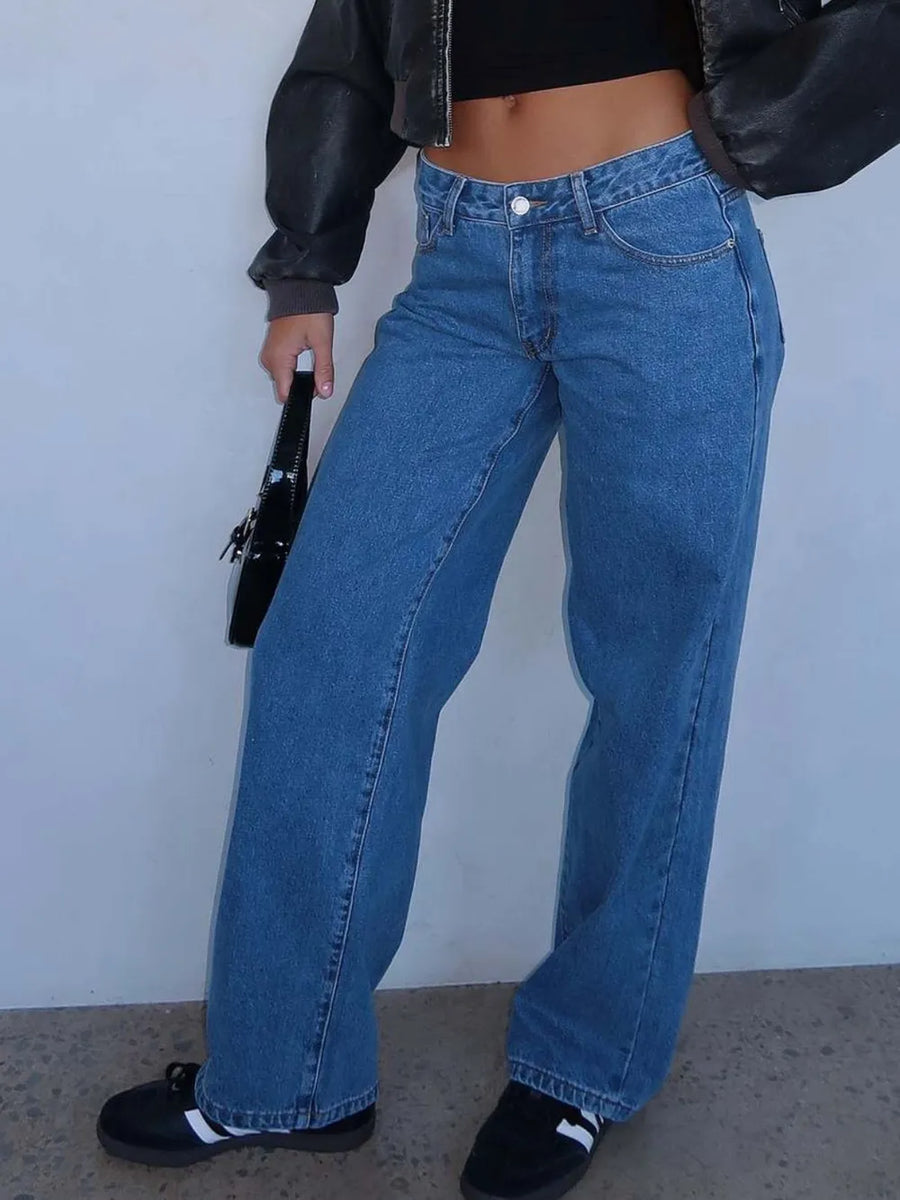 Person wearing blue jeans and a black jacket against a plain background