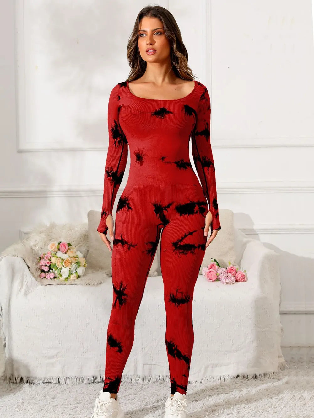 Woman wearing a red and black patterned outfit in a room with white walls and a white couch.