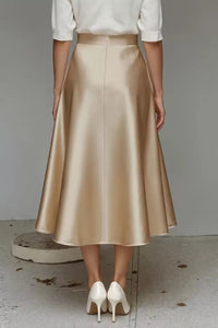 Person wearing a gold skirt and white shoes on a neutral background