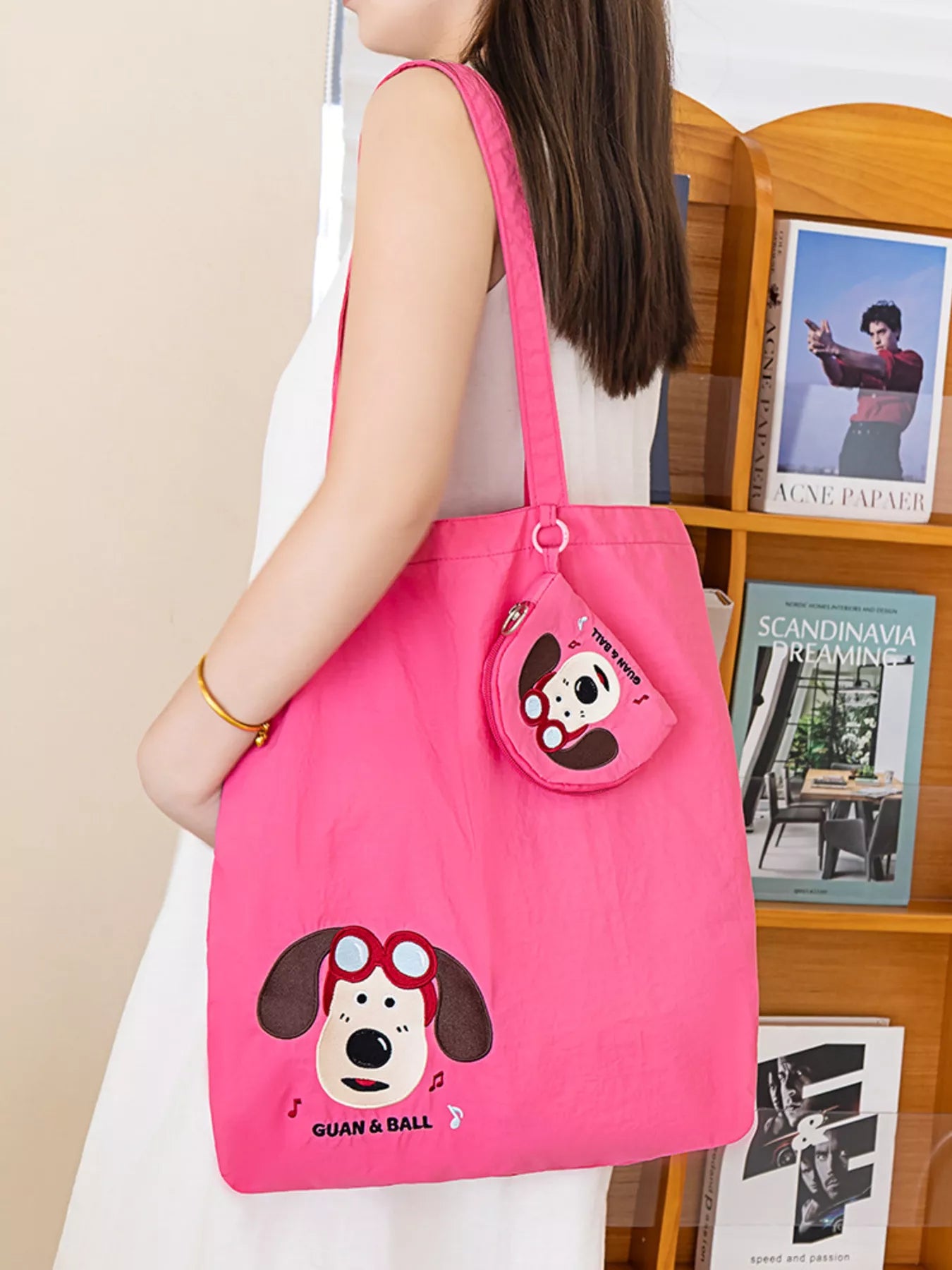 Person holding a pink tote bag with a cartoon dog design in front of a bookshelf.
