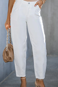 Person wearing white pants holding a beige handbag against a neutral background