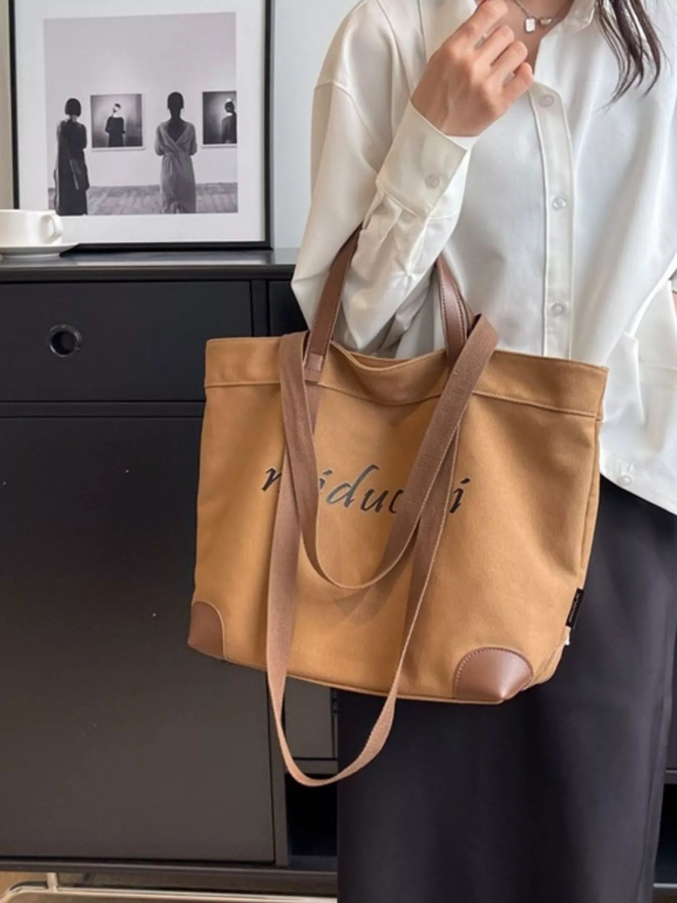 Person holding a brown leather tote bag with 'vidu' branding indoors.