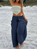 Person wearing a white top and blue pants on a sandy beach.