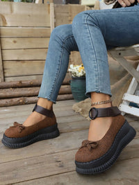 Brown platform shoes with black soles worn by a person sitting on a wooden bench.
