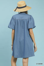Woman wearing a light denim dress and straw hat on a light blue background