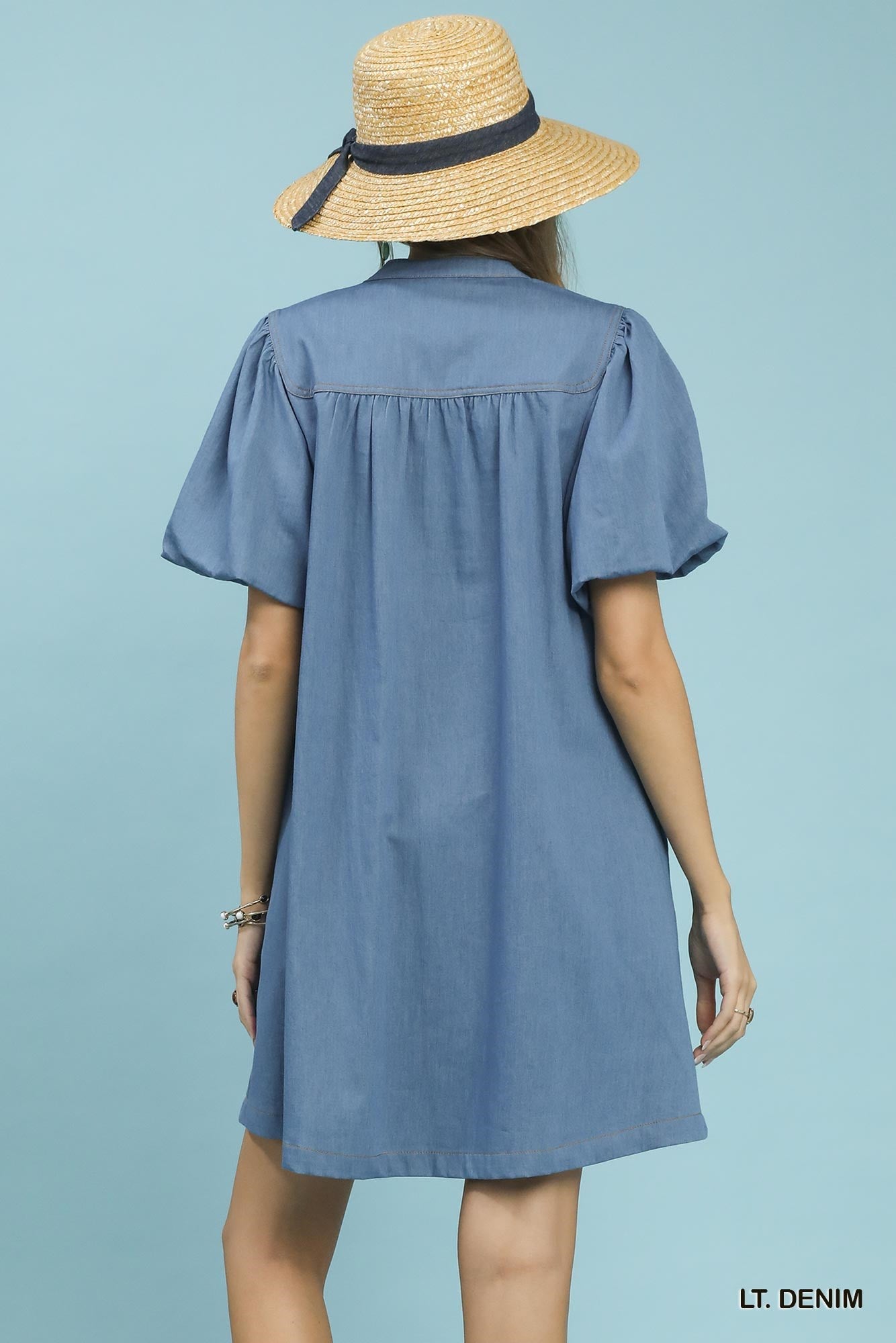 Woman wearing a light denim dress and straw hat on a light blue background
