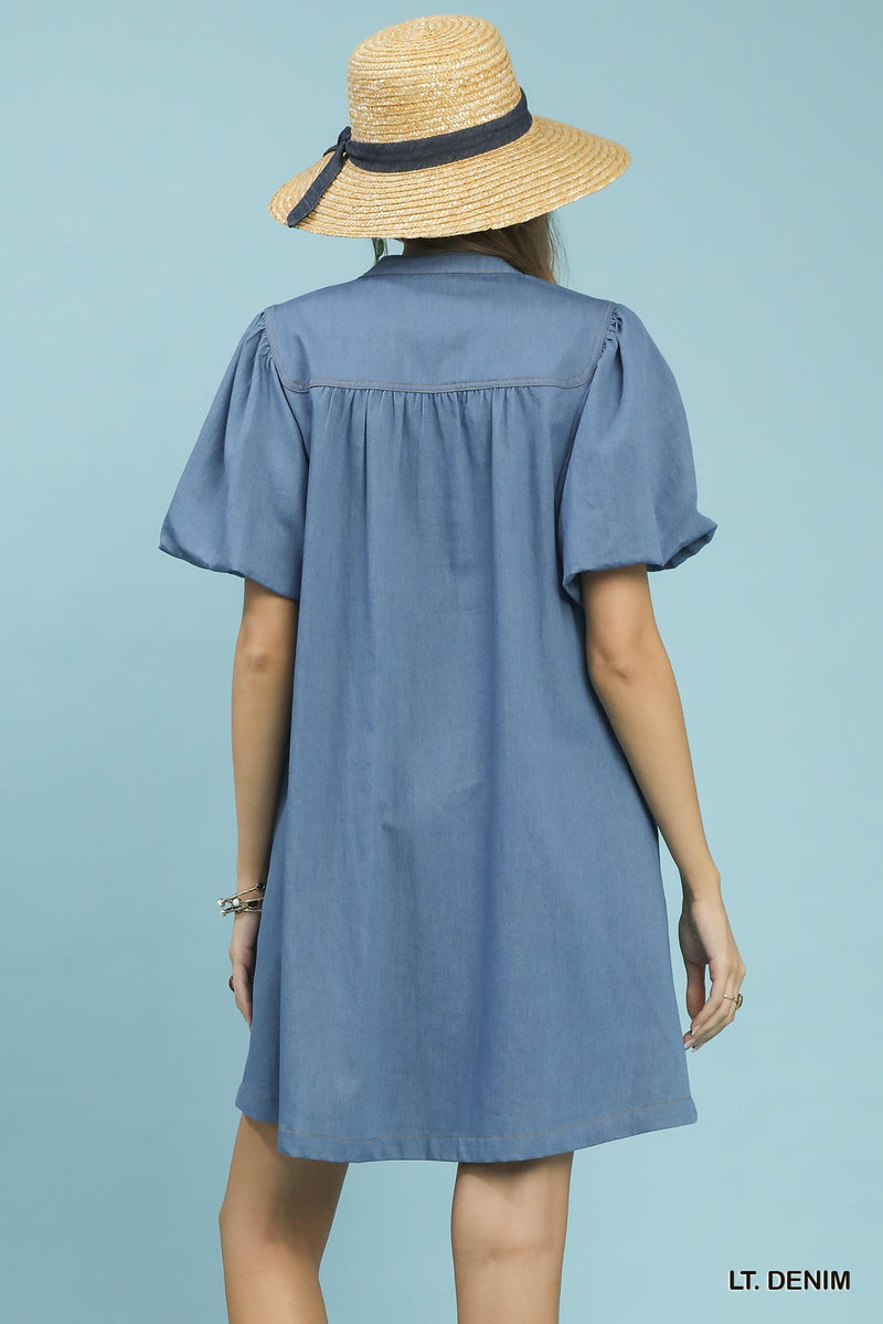 Woman wearing a light denim dress and straw hat on a light blue background