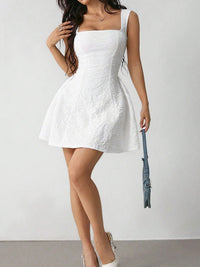 Woman wearing a white dress holding a blue handbag against a plain background