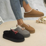 Three pairs of slippers (black, gray, brown) worn by a person on a textured surface.