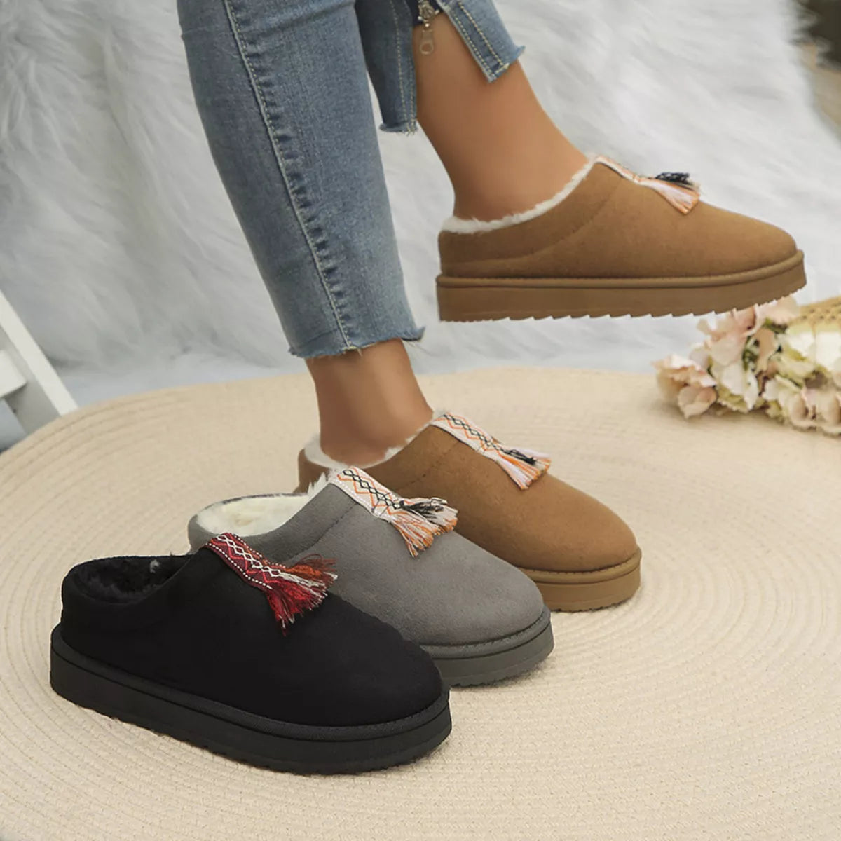 Three pairs of slippers (black, gray, brown) worn by a person on a textured surface.